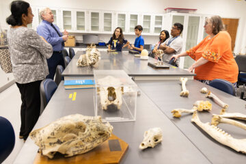 Photo of a biology instructor telling visitors about Bio Lab features with bones on a table in the foreground