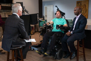 Photo of researcher Bolu Ajiboye and research participant Austin Beggin talking with Scott Pelley