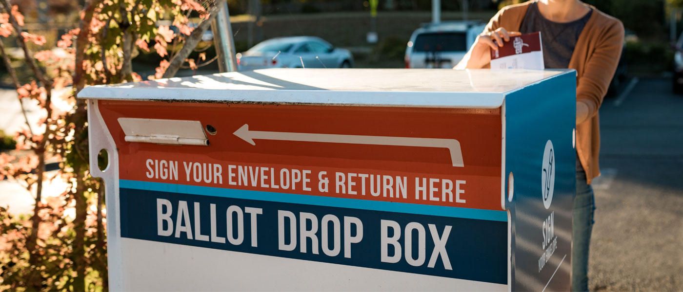 Photo of a person depositing an envelope into a ballot drop box