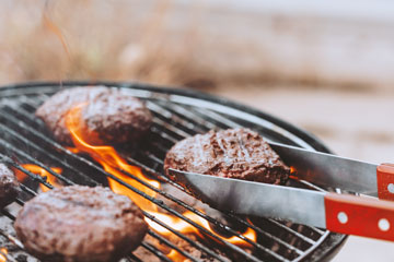 Photo of burgers on a grill with flames and tongs
