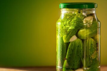 Pickled cucumbers in glass jars on green background