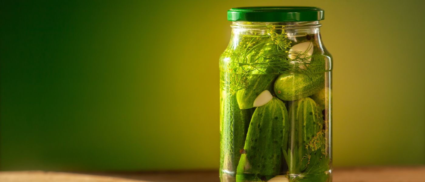 Pickled cucumbers in glass jars on green background