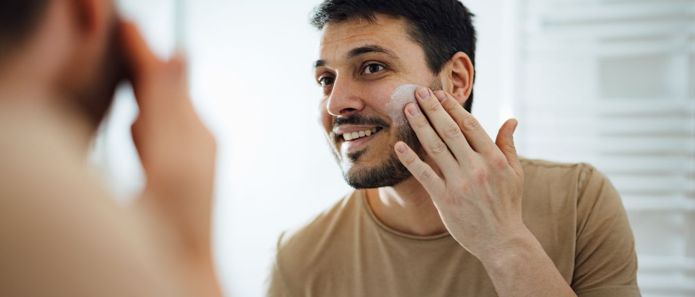 Happy man applying face cream in the bathroom