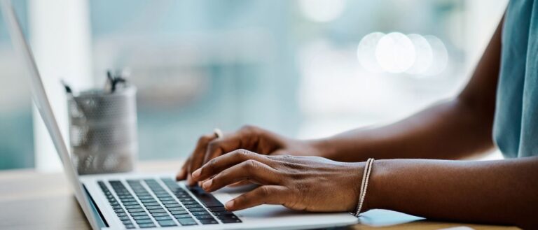 Closeup of a black businesswoman typing on a laptop keyboard in an office alone