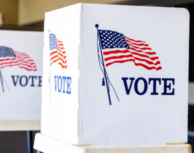 Photo of three empty voting booths with an American flag in the background