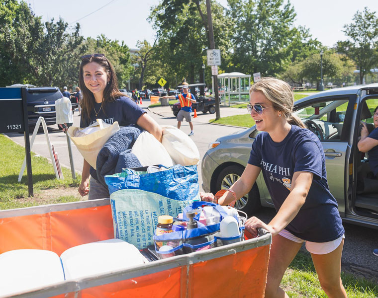 Two Case Western Reserve University students push a cart and carry belongings at move-in