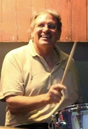 Photo of Bill Marx smiling as he plays the drums