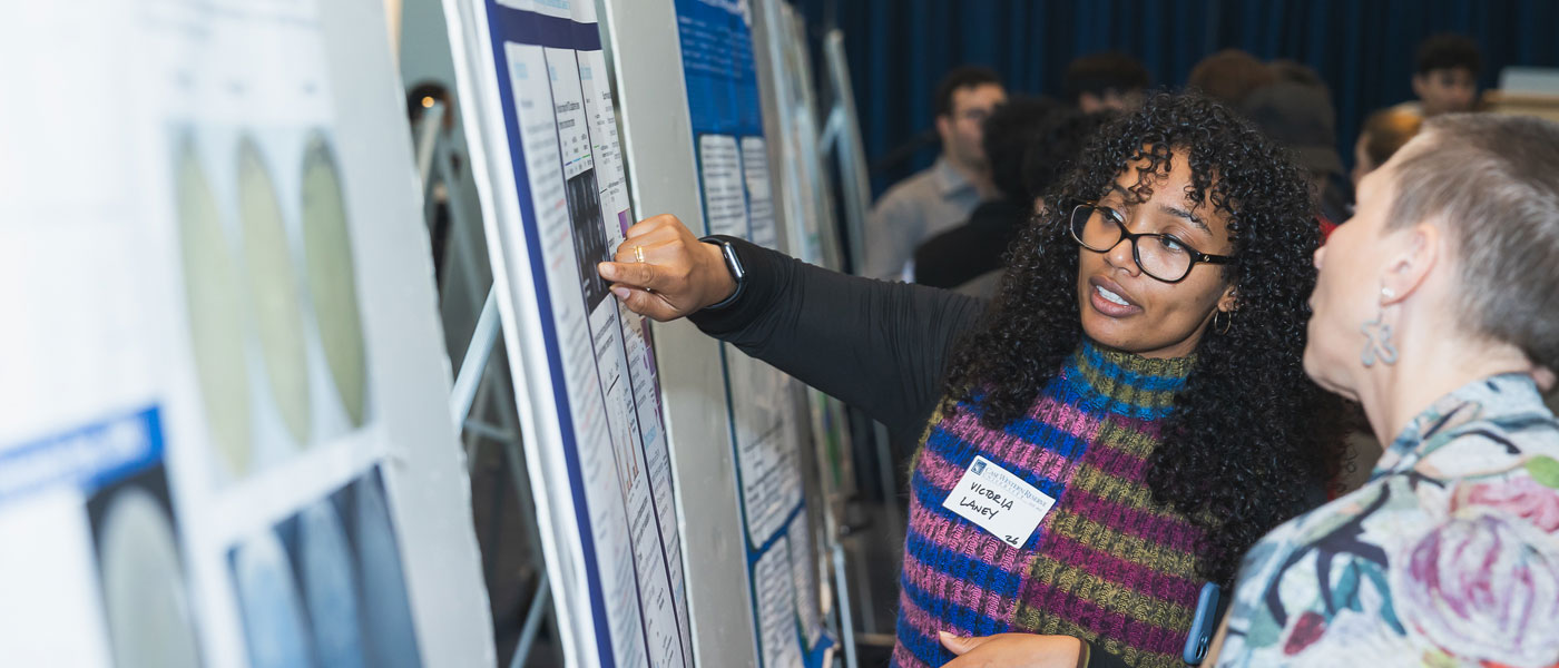 Photo of a student researcher presenting their work on a poster