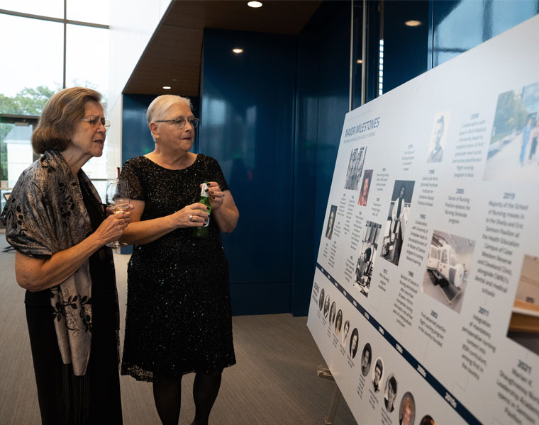 Guests at the nursing school's 100-year celebration looking at a large printed timeline of the school's history