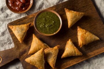 Close up of homemade Indian potato and lentil samosas with dipping chutneys