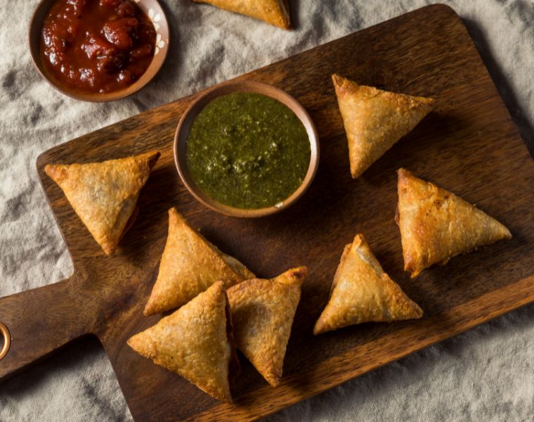 Close up of homemade Indian potato and lentil samosas with dipping chutneys