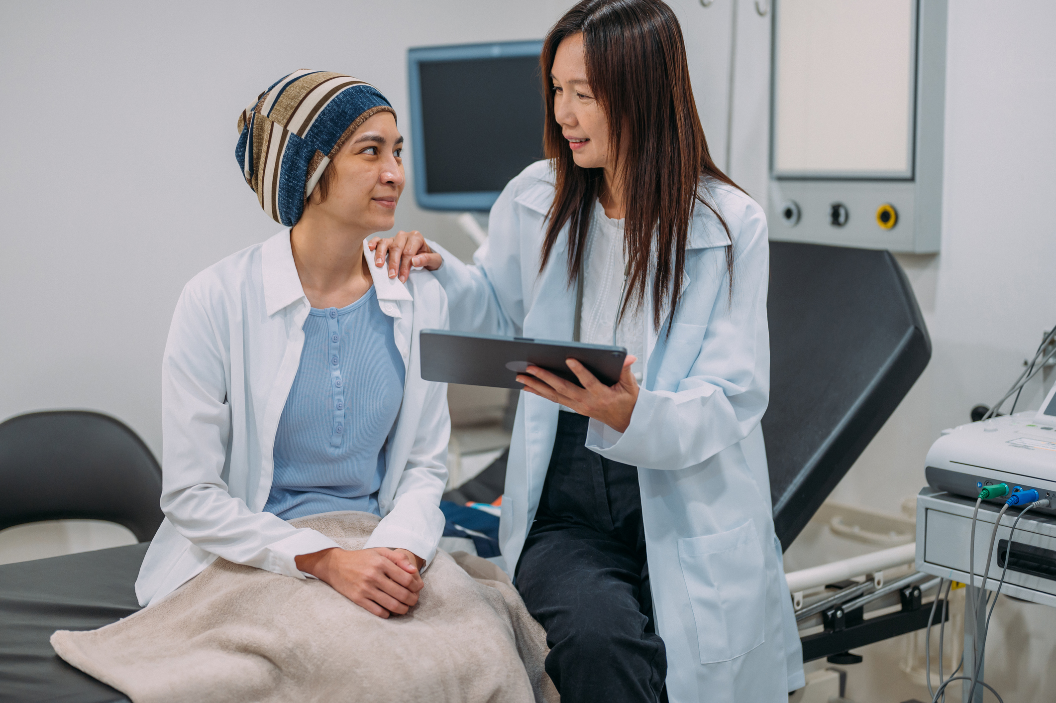 Photo of an Asian female gynecologist talking to her patient about cervical cancer awareness and test results on an electronic wireless tablet.