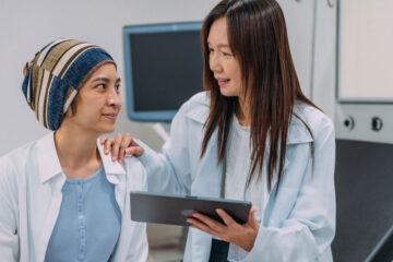 Photo of a doctor talking to a breast cancer patient while holding a tablet
