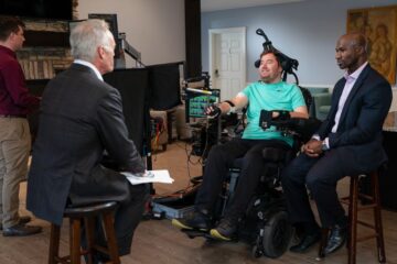 Photo of Bolu Ajiboye and research participant Austin Beggin talking with Scott Pelley during a "60 Minutes" segment