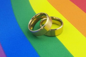 Gold wedding rings on LGBT pride flag. LGBT marriage concept. Courtesy of Getty Images.