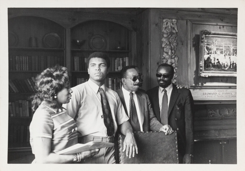 Black and white photo of Muhammad Ali surrounded by three others as he visits Karamu House in 1971
