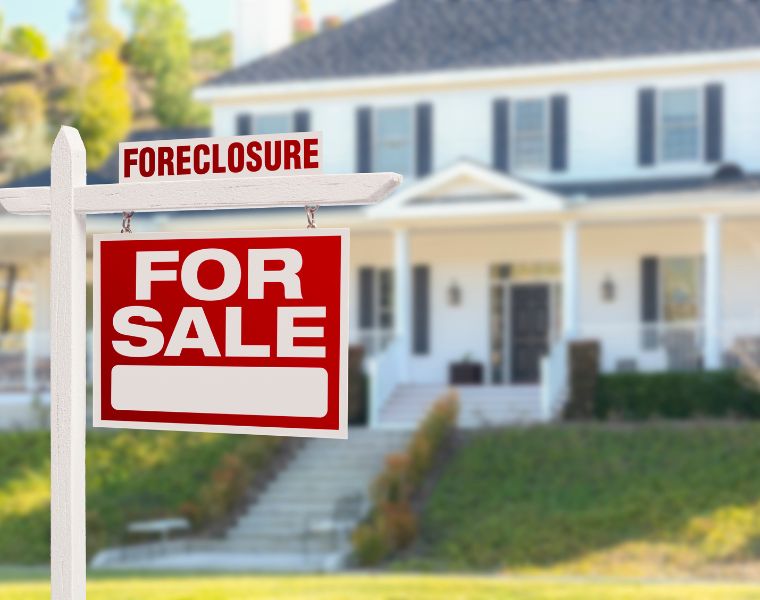 Foreclosure Home For Sale sign in front of a large house. Photography by Getty Images.