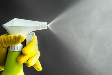 Photo of a gloved hand spraying a bottle of cleaning products