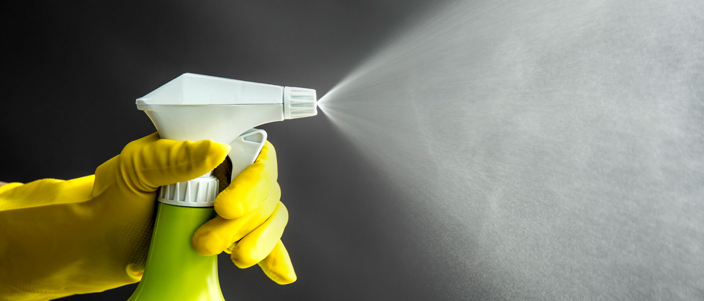 Photo of a gloved hand spraying a bottle of cleaning products