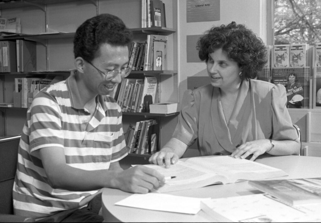Black and white image of Debbie Fatica and a student sitting at a table with books and papers in 1995
