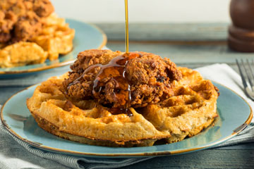 Photo of fried chicken on a waffle with syrup being poured over it