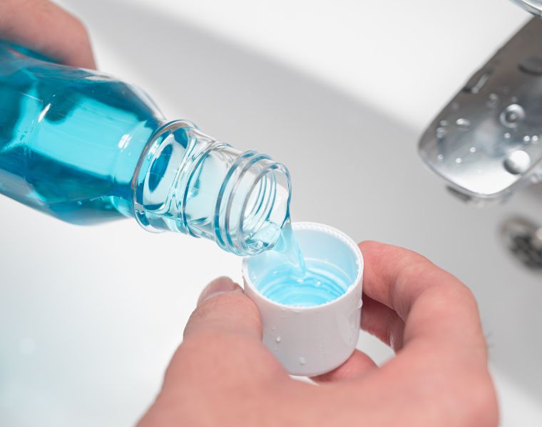 Close up of hands pouring mouthwash into cap. Courtesy of Getty Images.