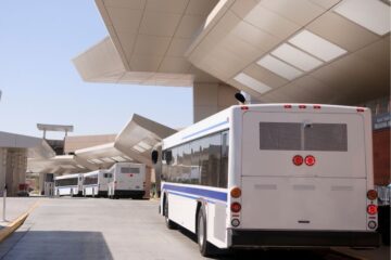 Line of buses at an airport rental car pickup area waiting to load passengers. Photography by Getty Images.