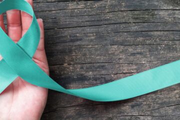 Teal ribbon awareness on woman's hand for Ovarian Cancer, Polycystic Ovary Syndrome (PCOS) disease, Post Traumatic Stress Disorder (PTSD), Tourette's Syndrome, Obsessive Compulsive Disorder (OCD). Courtesy of Getty Images.