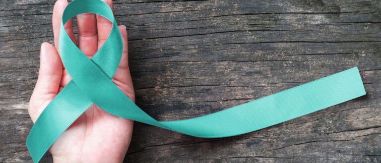 Teal ribbon awareness on woman's hand for Ovarian Cancer, Polycystic Ovary Syndrome (PCOS) disease, Post Traumatic Stress Disorder (PTSD), Tourette's Syndrome, Obsessive Compulsive Disorder (OCD). Courtesy of Getty Images.