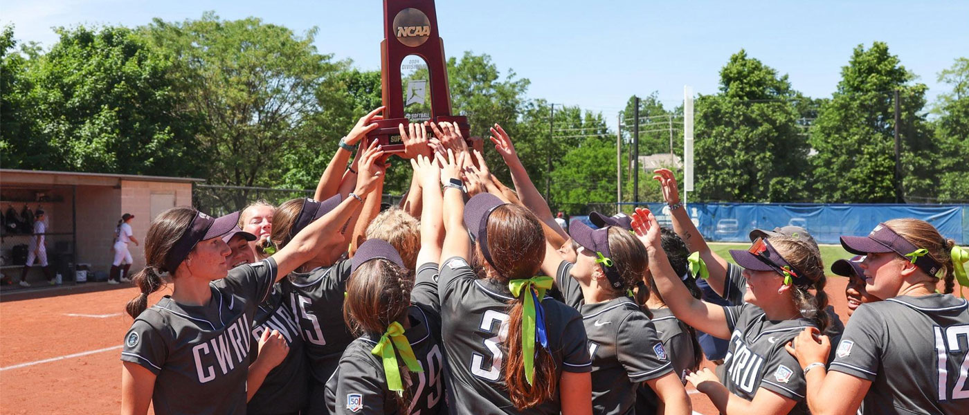 Case Western Reserve University softball players huddle together and hold up an NCAA trophy