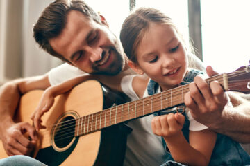 Father with daughter on his lap teaching her guitar