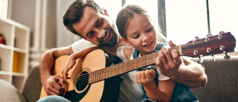 Father with daughter on his lap teaching her guitar