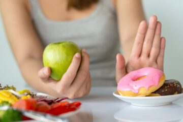Young woman rejecting unhealthy food such as donut or dessert and choosing healthy food such as fresh fruit or vegetable. Photography by Getty Images.