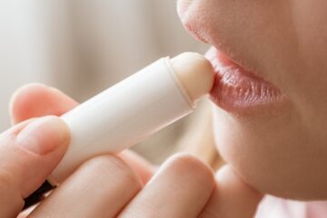Photo of young woman applying moisturizing balm to her lips.