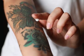 Closeup of a woman applying cream on her arm with tattoos.