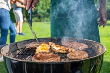 Mid section of man turning burgers and meat on barbecue grill in garden.