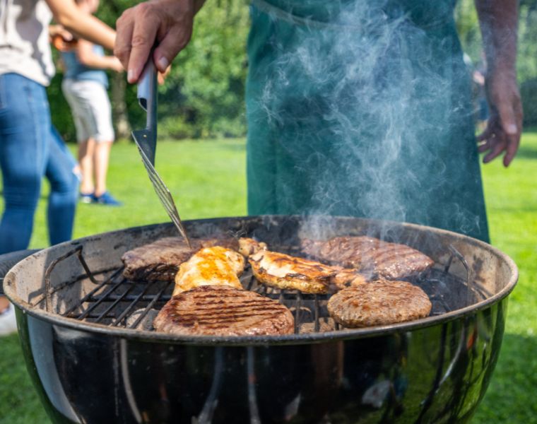 Mid section of man turning burgers and meat on barbecue grill in garden.