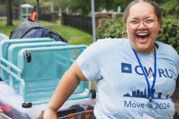 Photo of an enthusiastic CWRU volunteer pulling a cart full of a new student's belongings during a rainy move-in day