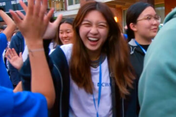 Photo of a new CWRU student high-fiving orientation leaders on DiSanto Field ahead of tradition