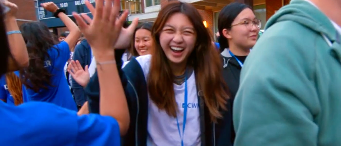 Photo of a new CWRU student high-fiving orientation leaders on DiSanto Field ahead of tradition