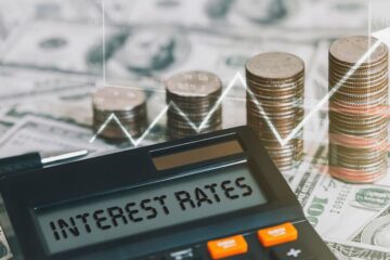 The word interest rate is on a calculator with a coin, a graph, and an arrow pointing up. Concepts of raising interest rates, economic conditions, inflation, etc.