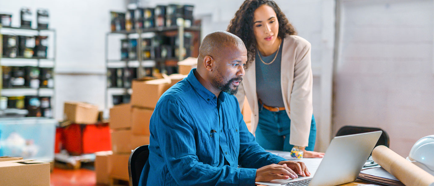 Photo of two colleagues working together at a laptop with boxes behind them in an office