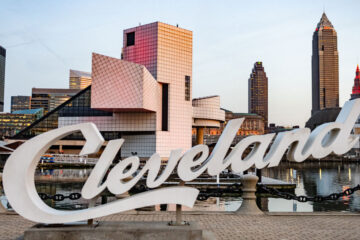 Photo of the script Cleveland sign with the Rock & Roll Hall of Fame and Downtown Cleveland in the background