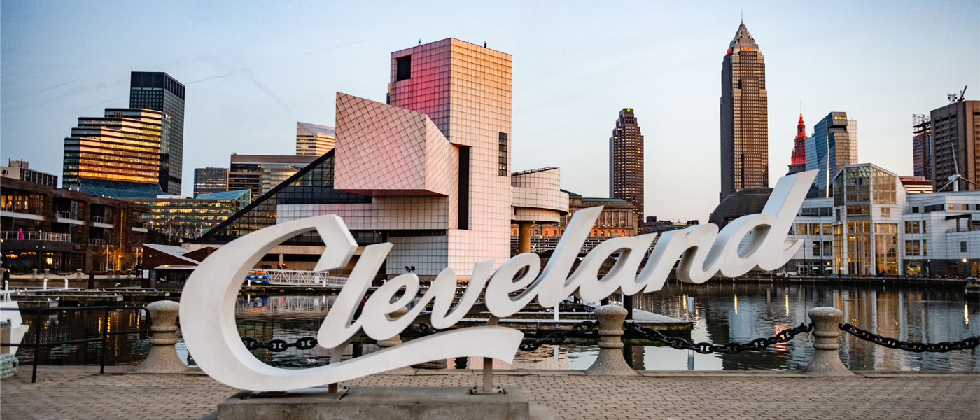 Photo of the script Cleveland sign with the Rock & Roll Hall of Fame and Downtown Cleveland in the background