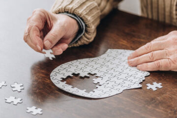 Photo of an elderly person putting together a puzzle in the shape of a head with all-white pieces