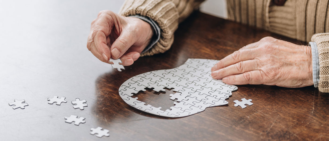 Photo of an elderly person putting together a puzzle in the shape of a head with all-white pieces