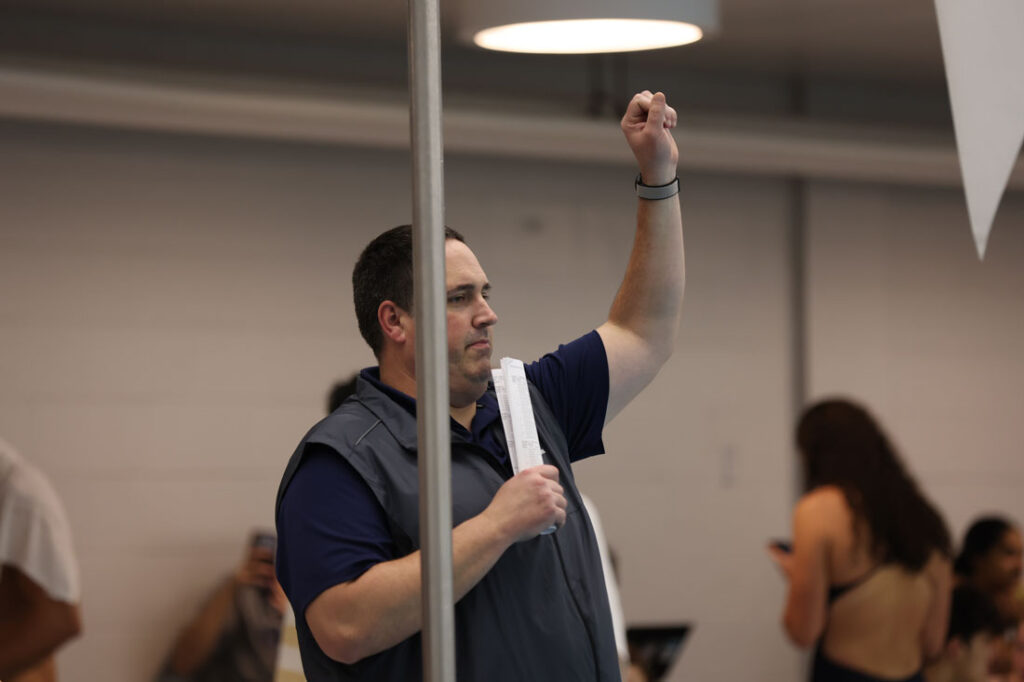 Photo of Doug Milliken during a swimming and diving meet watching on the sidelines with an arm in the air