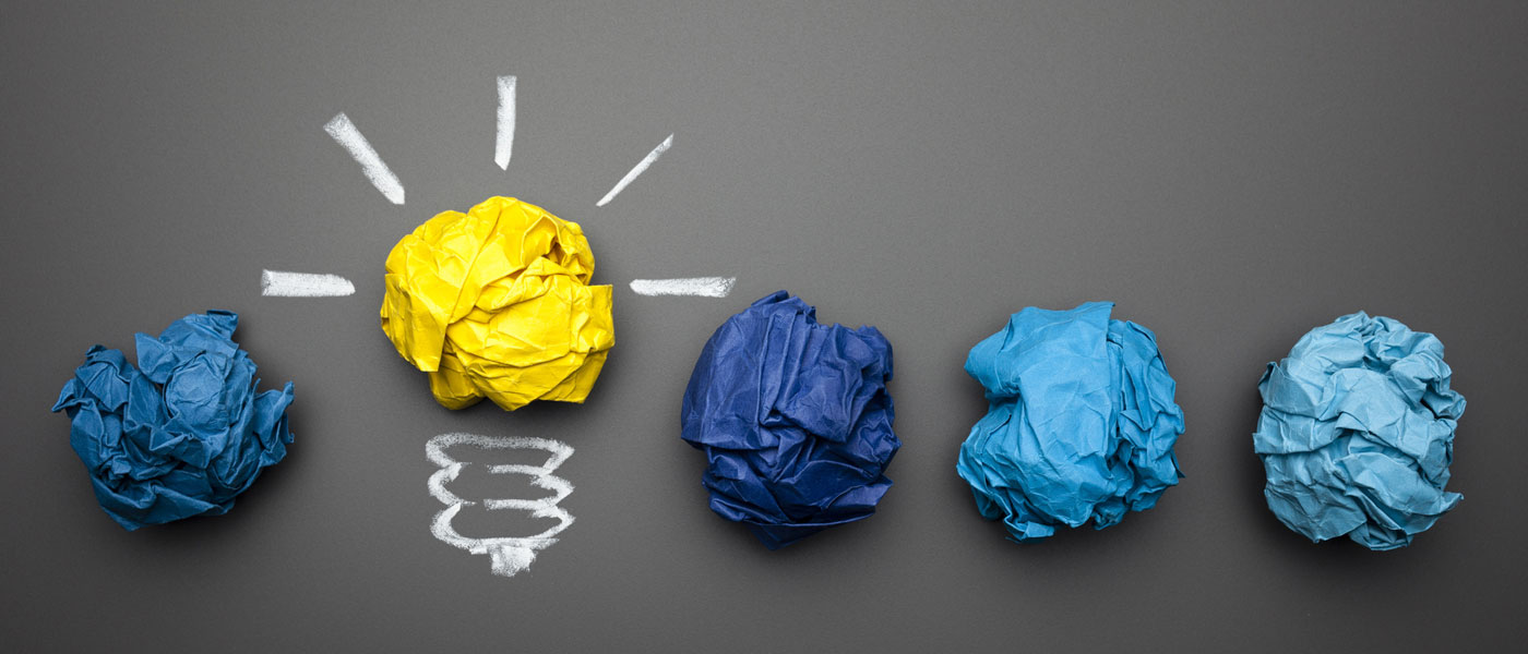 Line of five crumpled balls of paper, with one in yellow and a drawing around it to make it look like a light bulb