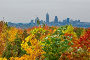 Photo of fall foliage in reds, yellows, oranges and greens with a distant view of the Cleveland skyline in the background