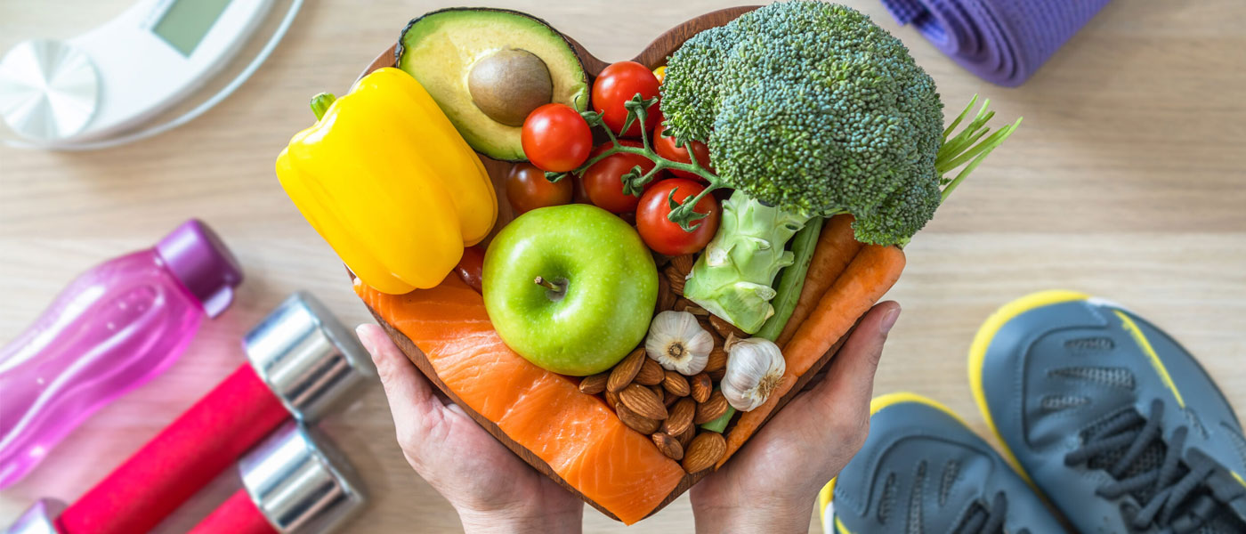 Photo of someone holding a heart-shaped dish full of nutritious foods with water bottles, tennis shoes and weights on the floor